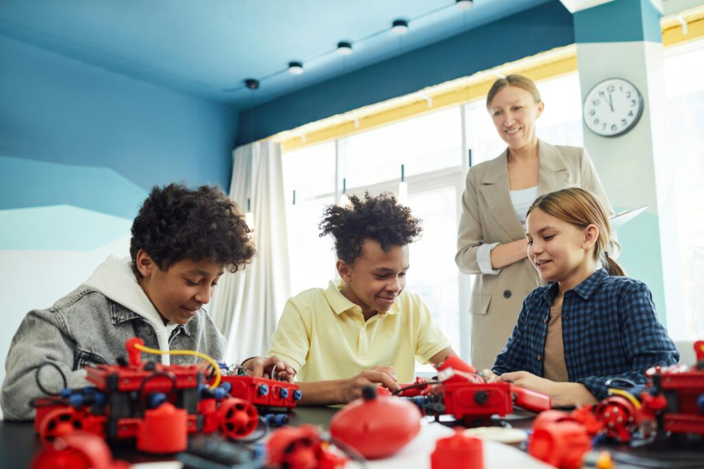 pexels-photo-7869086-7869086 Smiling students collaborating on a robotics project under teacher's guidance in a classroom setting.