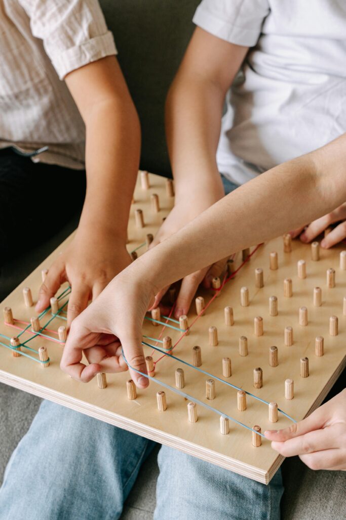 pexels-photo-8504340-8504340 Children enjoy a mindful activity with a wooden geoboard, using colorful rubber bands.