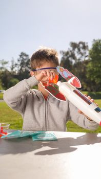 Young boy prepares a rocket experiment in a park, enjoying a playful outdoor activity.